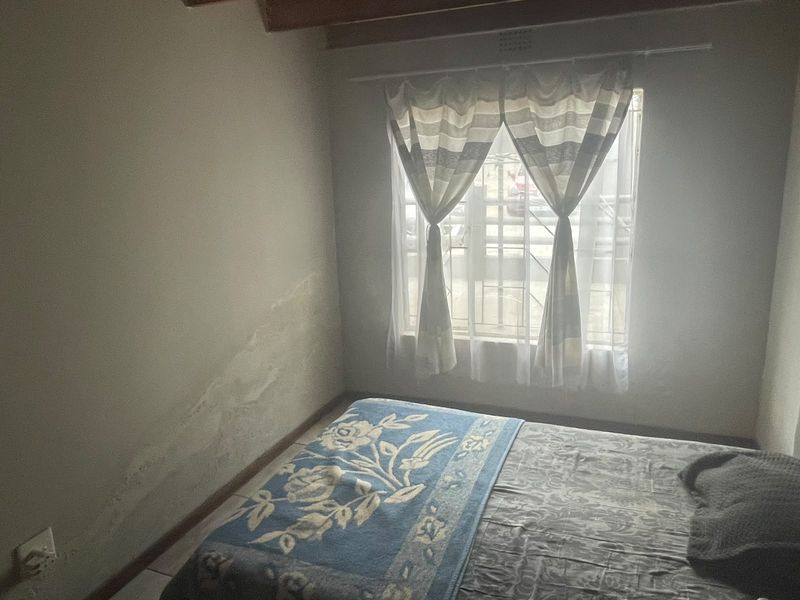 A bedroom featuring exposed timber ceiling beams and security bars on the window, showing signs of wall dampness requiring attention.