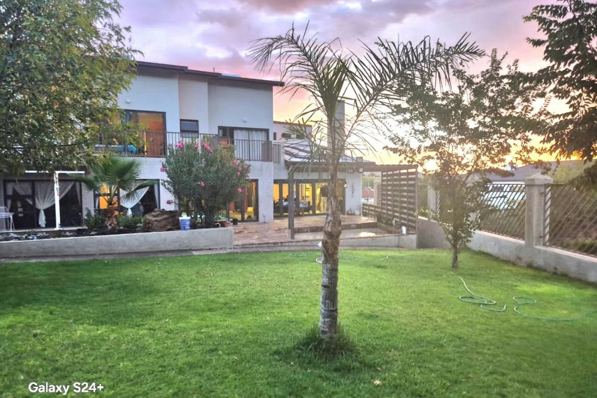 A rear view of the property featuring a landscaped lawn, a paved patio area with a pergola, and an upper-level balcony at sunset.