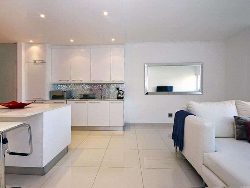 Modern open-plan living area featuring a sleek kitchen with white cabinetry, mosaic backsplash, and a central island, complemented by polished tiled flooring.