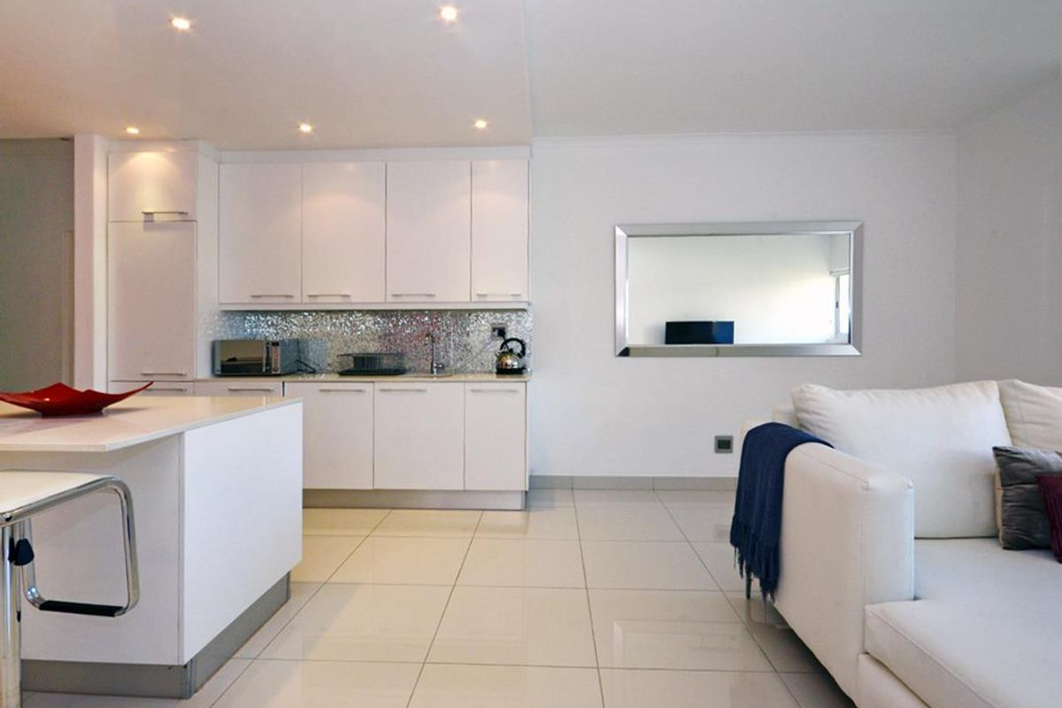 Modern open-plan living area featuring a sleek kitchen with white cabinetry, mosaic backsplash, and a central island, complemented by polished tiled flooring.