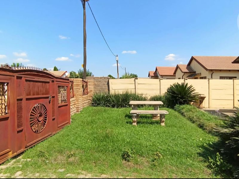 A rear garden area featuring a lawn, precast concrete boundary walls, and a large metal gate.