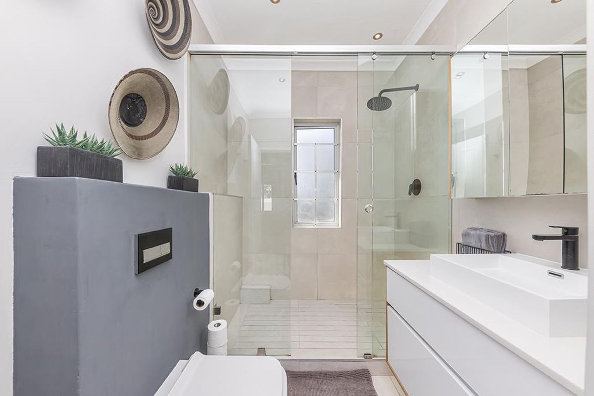 Modern bathroom featuring a walk-in glass shower with a rain shower head, wall-mounted toilet, and a sleek vanity with a black mixer tap.