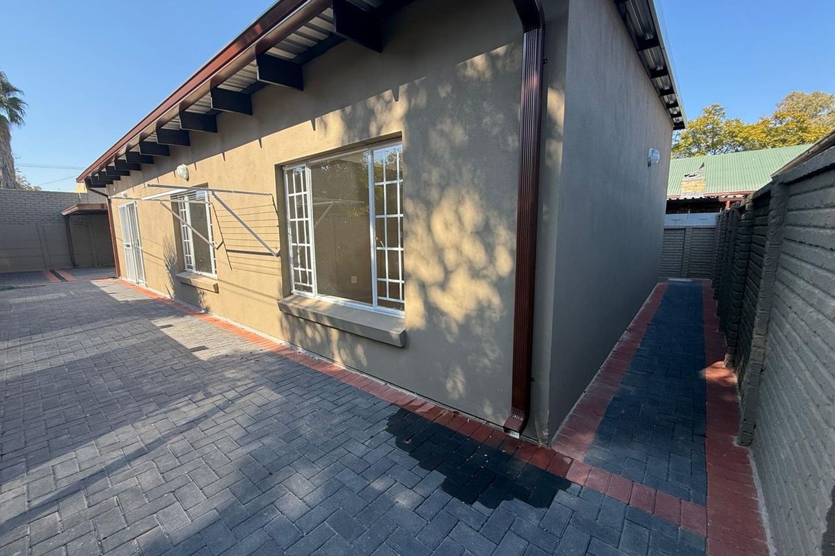 A view of the rear exterior of the house, featuring paved walkways, a plastered facade, and a metal roof structure.