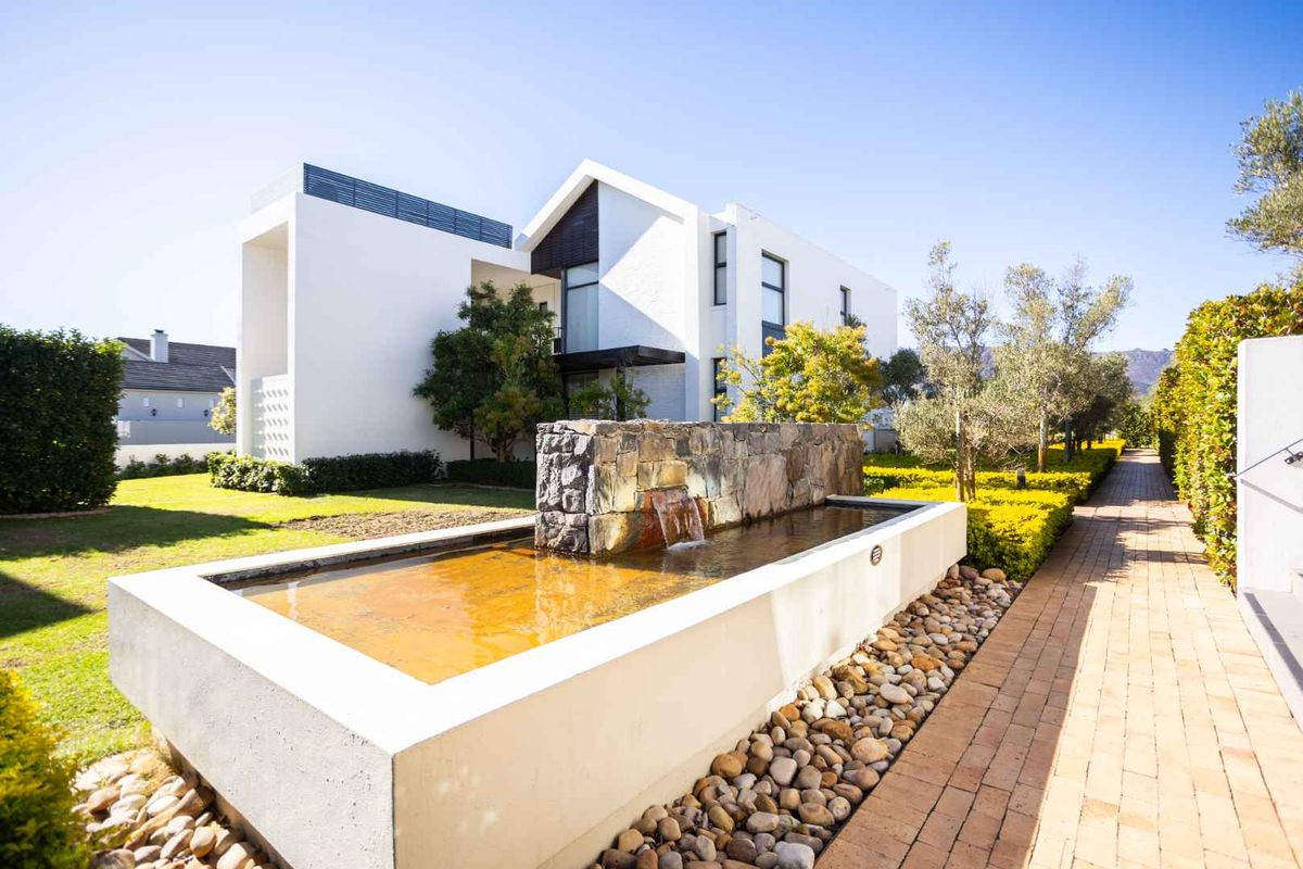 A beautifully landscaped rear garden featuring a modern stone water feature, brick pathways, and a contemporary white architectural building facade.