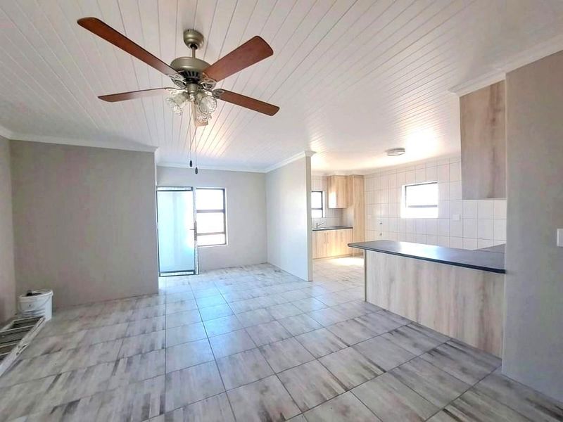 Spacious open-plan living and kitchen area featuring modern tiled flooring, a ceiling fan, and neutral cabinetry with a breakfast bar.