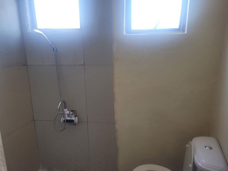 A compact bathroom featuring a shower area with tiled walls, a standard toilet, and two small windows providing natural light.