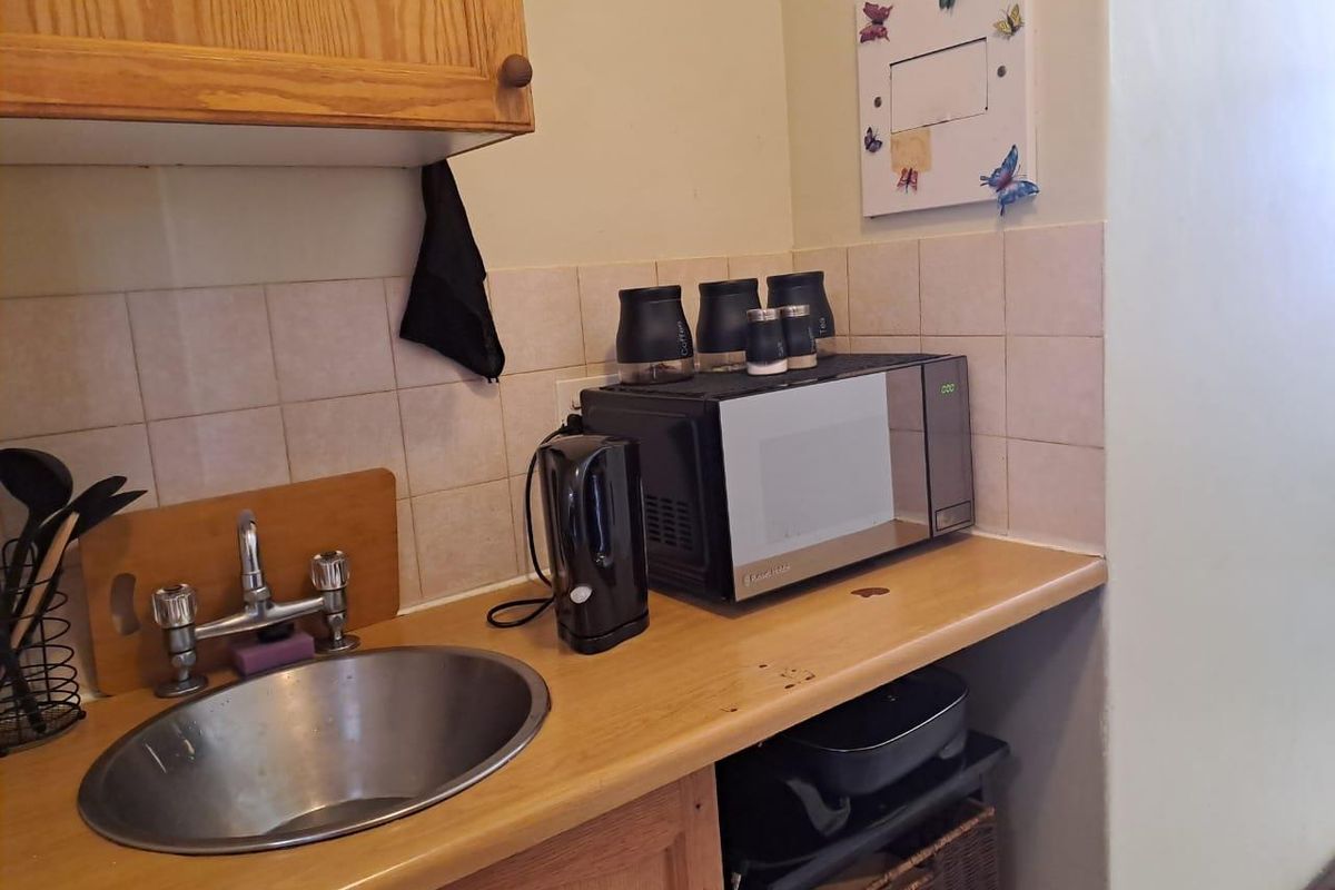A compact kitchen area featuring wooden cabinetry, a stainless steel sink, and a tiled backsplash, showing signs of wear on the countertop.