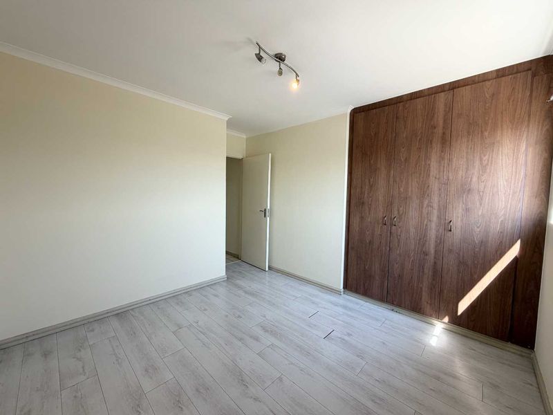 A bright, empty bedroom featuring light-toned laminate flooring and dark wood-finish built-in cupboards.