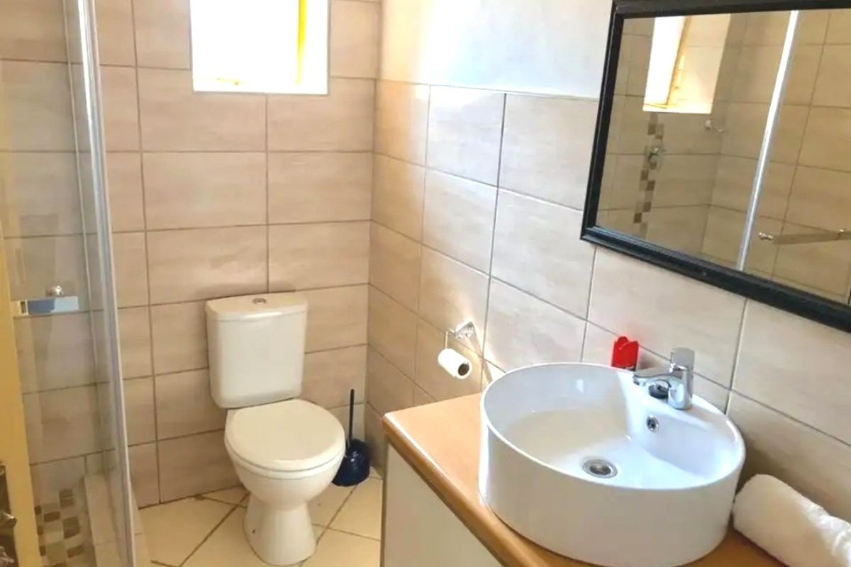 A functional bathroom featuring a shower enclosure, a modern vessel sink on a vanity cabinet, and neutral ceramic tiling throughout.