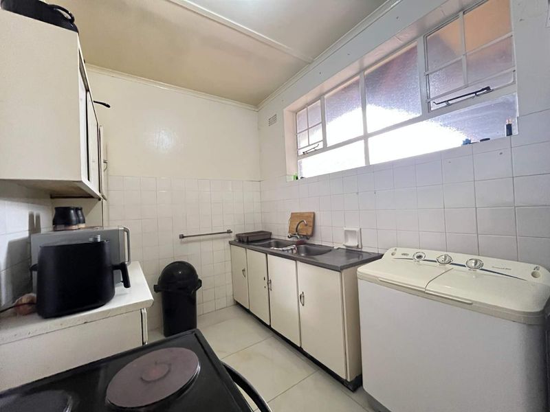 A functional laundry area featuring built-in cabinetry, a stainless steel sink, and tiled splashbacks, offering a practical space for utility tasks.