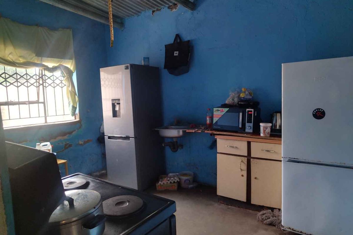 A basic kitchen area featuring a sink, built-in cabinetry, and exposed corrugated metal ceiling with significant wall finish deterioration.