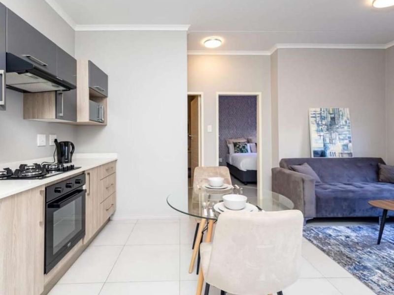 Modern open-plan apartment featuring a sleek kitchen with built-in appliances, tiled flooring, and a seamless flow into the living and dining area.