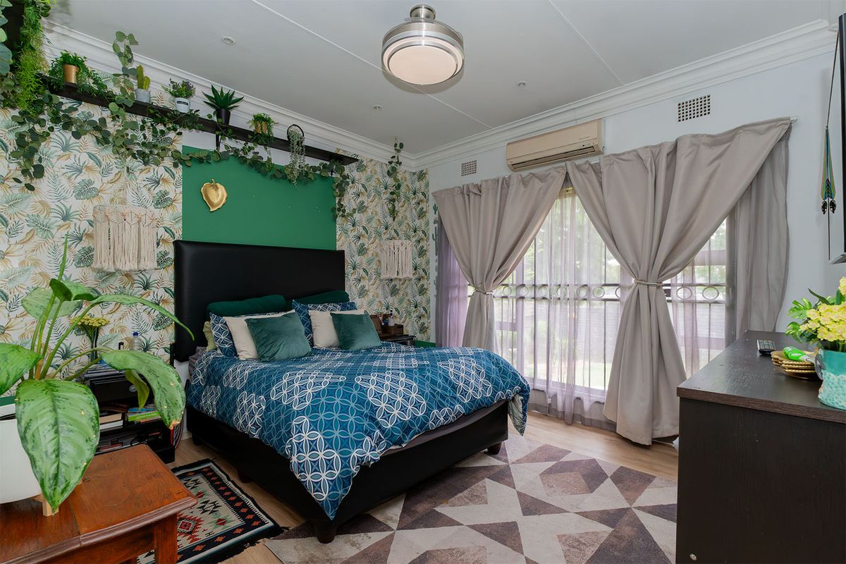 A well-maintained bedroom featuring laminate flooring, a split-system air conditioner, and sliding glass doors with security gate access.
