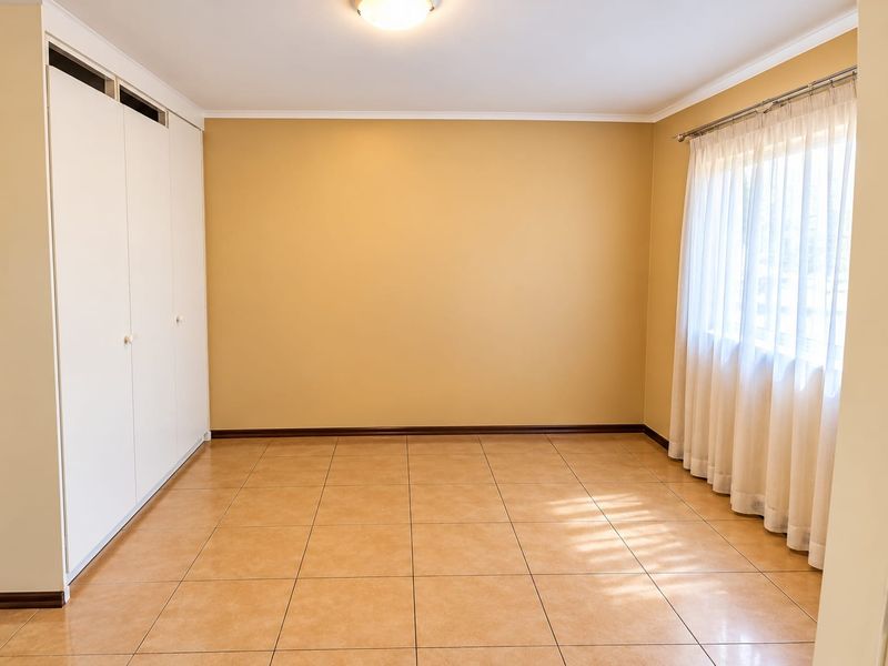 A clean, empty bedroom featuring neutral wall paint, ceramic floor tiles, and built-in storage cupboards.