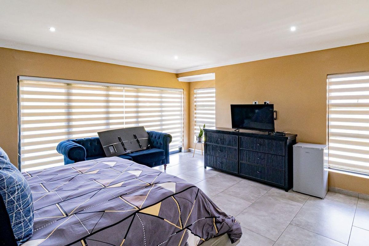 Spacious bedroom featuring large windows with fitted blinds, neutral wall tones, and modern tiled flooring throughout.