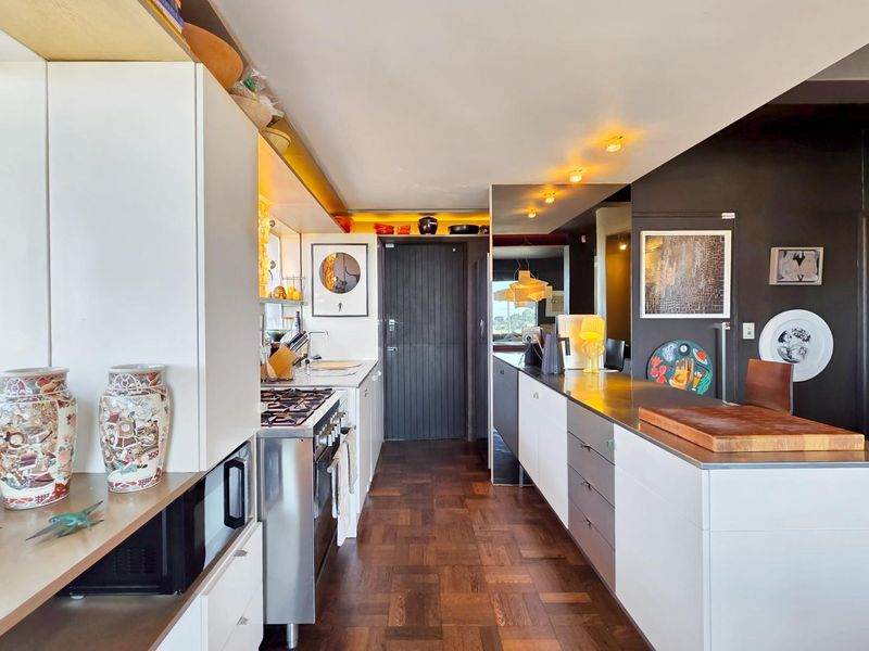 Modern kitchen featuring high-end cabinetry, stainless steel countertops, a gas stove, built-in microwave, and rich parquet flooring with integrated lighting.