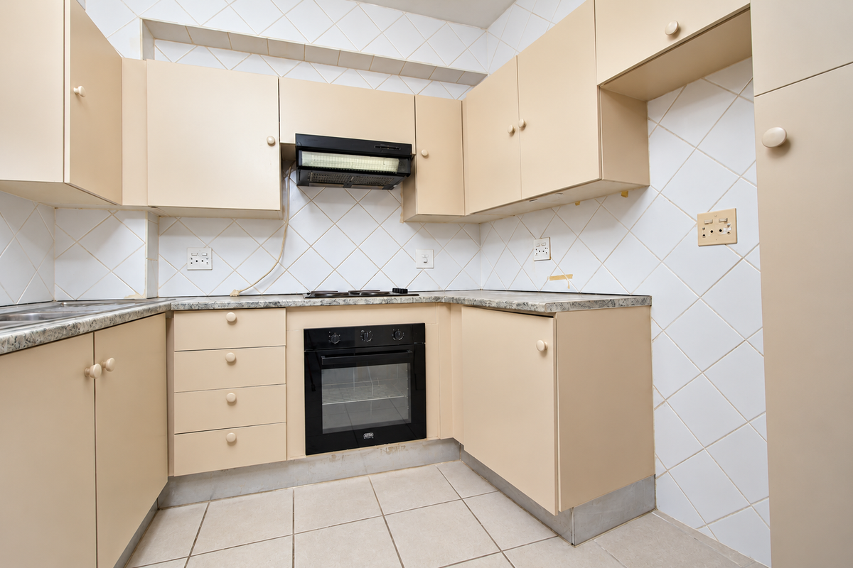 A dated kitchen featuring built-in cabinetry, laminate countertops, an integrated oven, and a tiled backsplash, offering a functional layout ready for modernization.