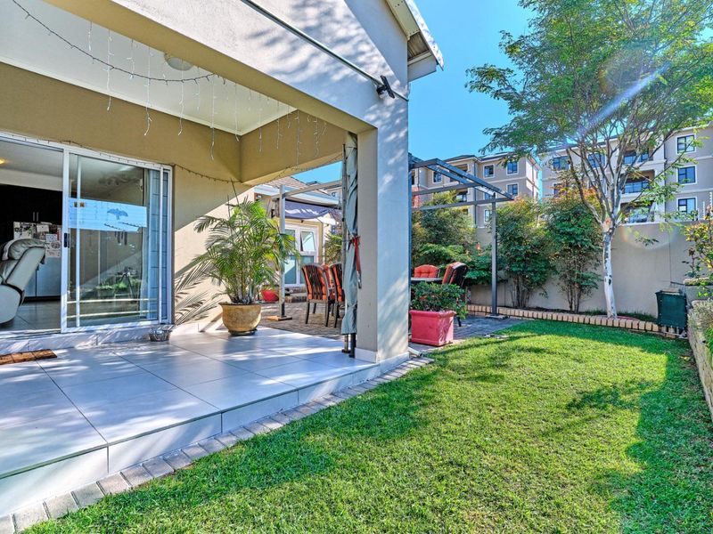 A covered tiled patio area leading out to a private garden with a lawn and brick boundary wall.