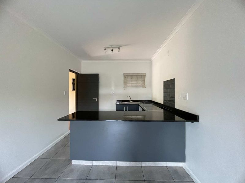 A clean, modern kitchen featuring dark cabinetry, granite countertops, a subway tile backsplash, and neutral tiled flooring in an open-plan layout.
