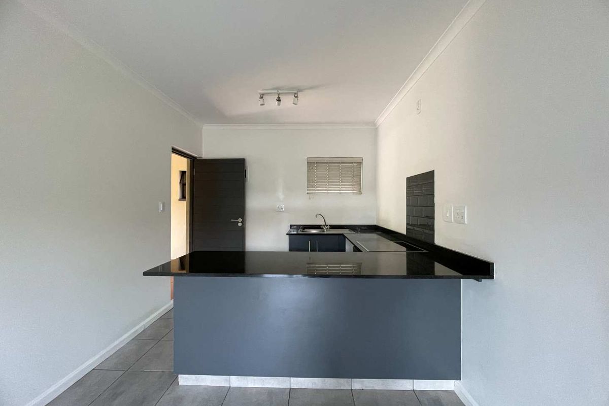 A clean, modern kitchen featuring dark cabinetry, granite countertops, a subway tile backsplash, and neutral tiled flooring in an open-plan layout.