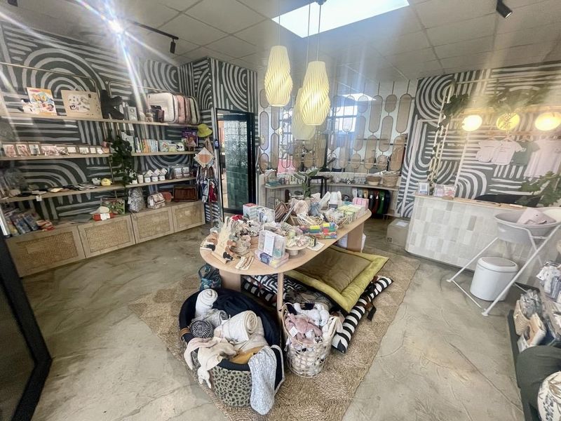 A retail space featuring built-in shelving, a reception counter, pendant lighting, and polished concrete flooring, currently set up as a boutique shop.