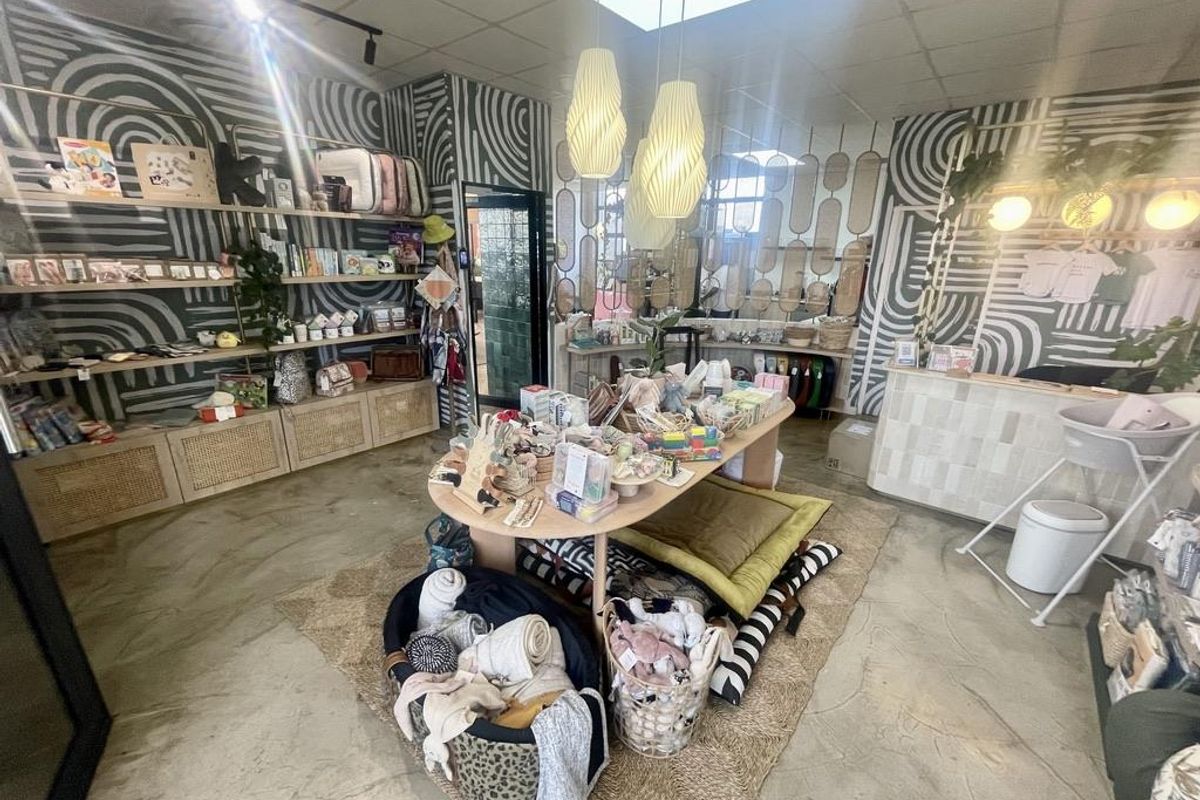 A retail space featuring built-in shelving, a reception counter, pendant lighting, and polished concrete flooring, currently set up as a boutique shop.