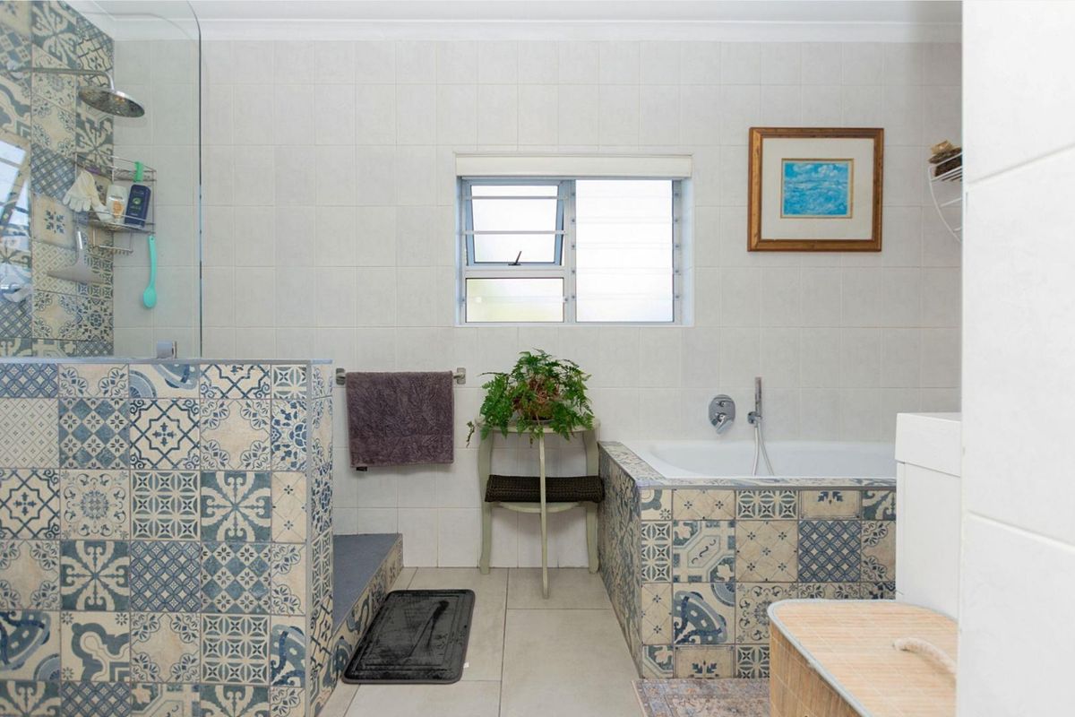A bathroom featuring a tiled walk-in shower, a built-in bathtub with decorative patterned tiles, and a window for natural light.