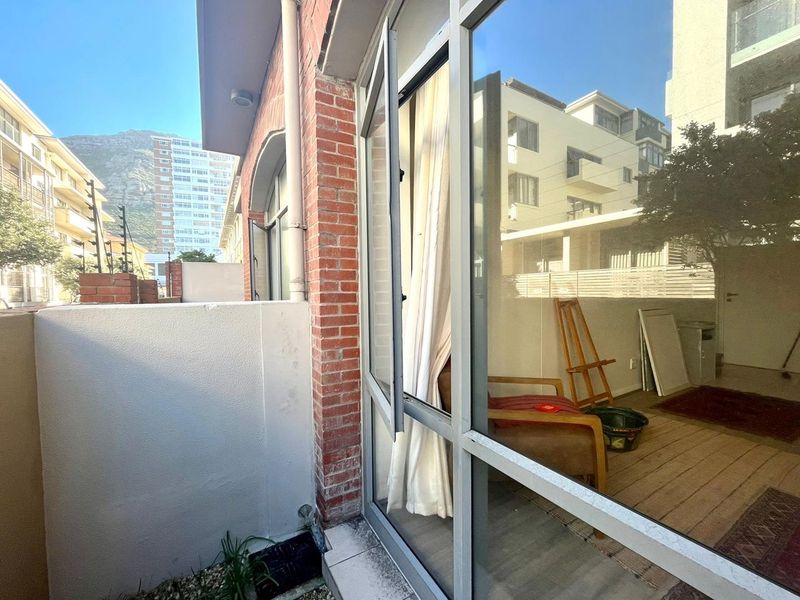 A compact balcony area featuring a brick facade, aluminium-framed windows, and a concrete parapet wall, offering a view of the surrounding urban environment.