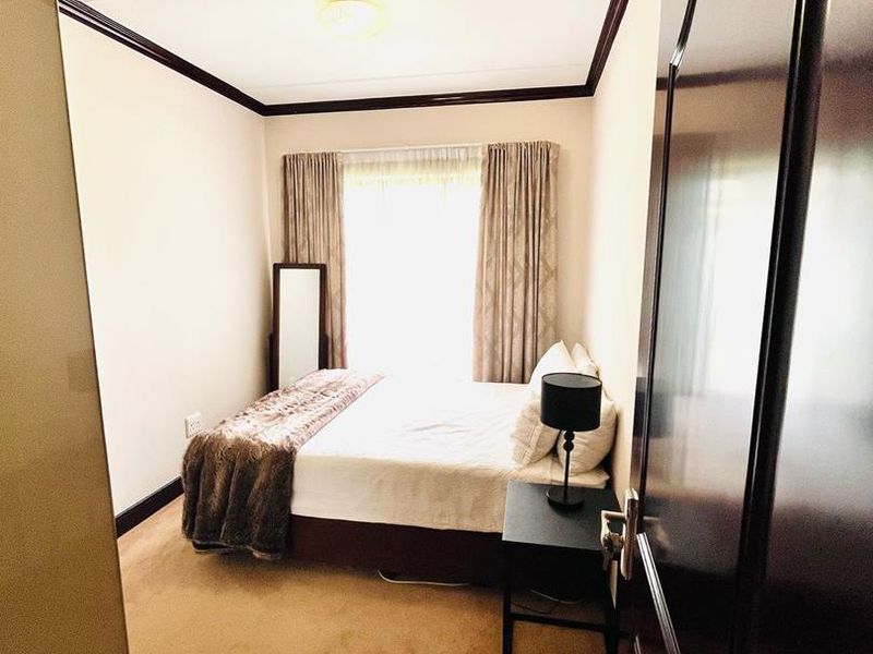 A cozy bedroom featuring carpeted flooring, dark crown molding, and natural light from the window.