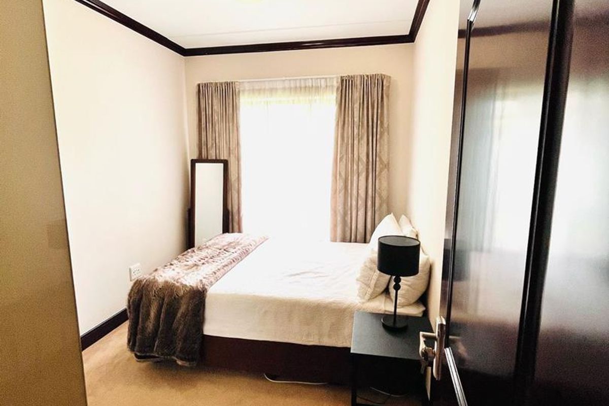 A cozy bedroom featuring carpeted flooring, dark crown molding, and natural light from the window.
