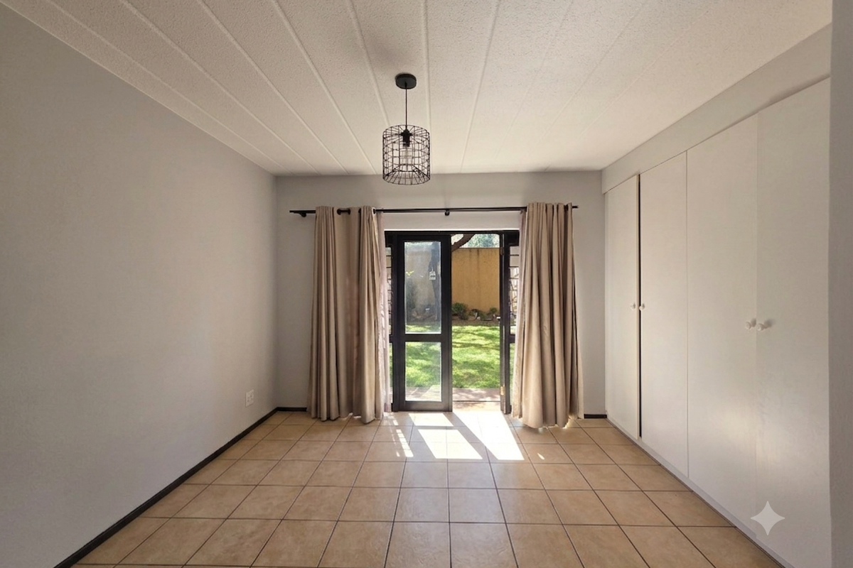A bright, empty bedroom featuring neutral tiled flooring, ample built-in cupboard storage, and direct access to a private garden area through a glass door.