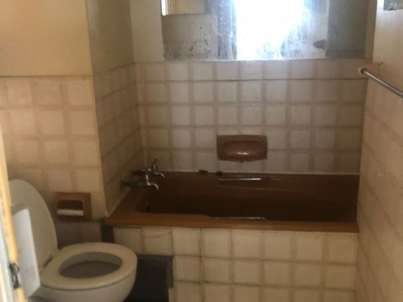 A dated bathroom featuring a built-in bathtub, ceramic tiling, and standard toilet, requiring modernization to improve its overall condition and appeal.