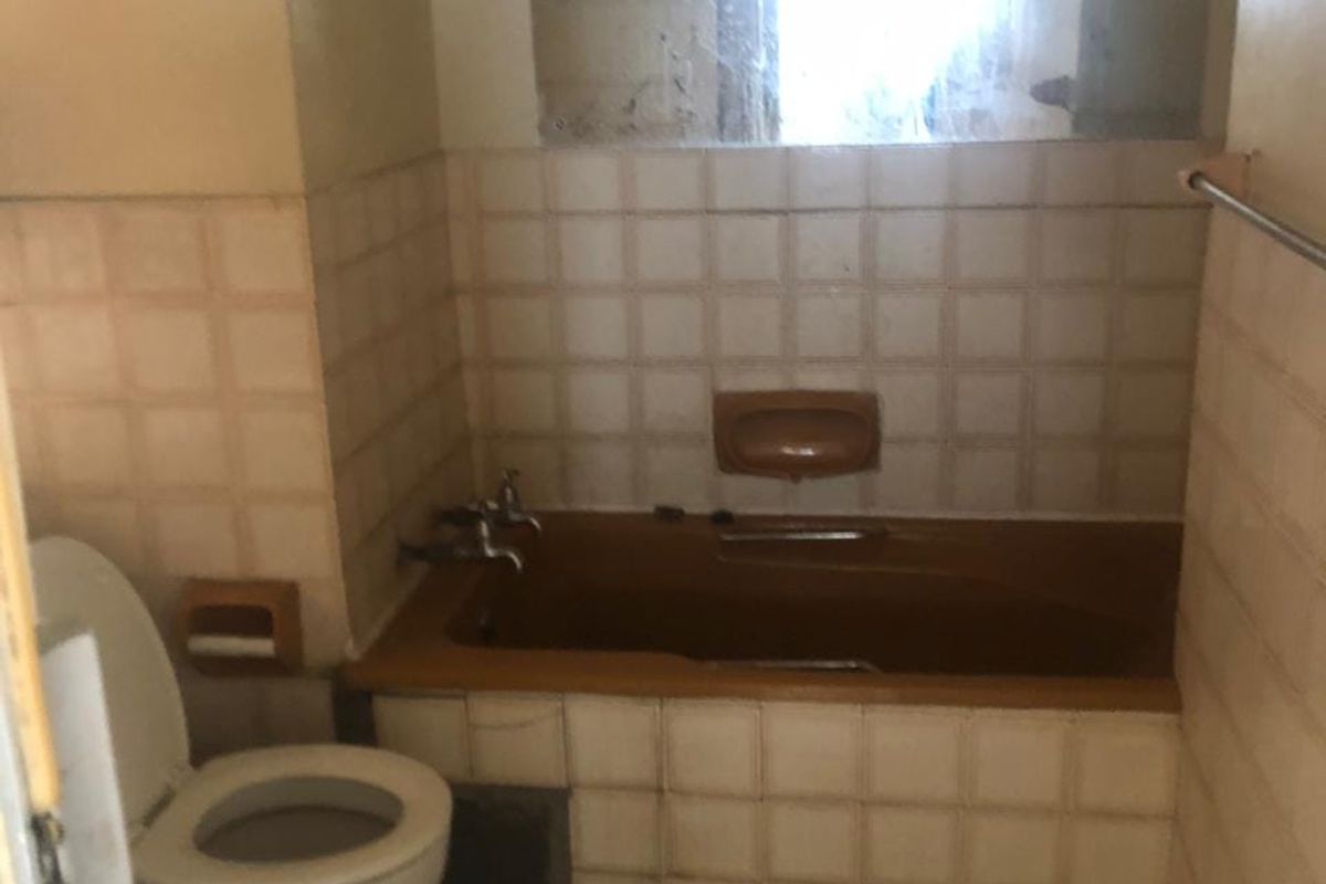 A dated bathroom featuring a built-in bathtub, ceramic tiling, and standard toilet, requiring modernization to improve its overall condition and appeal.