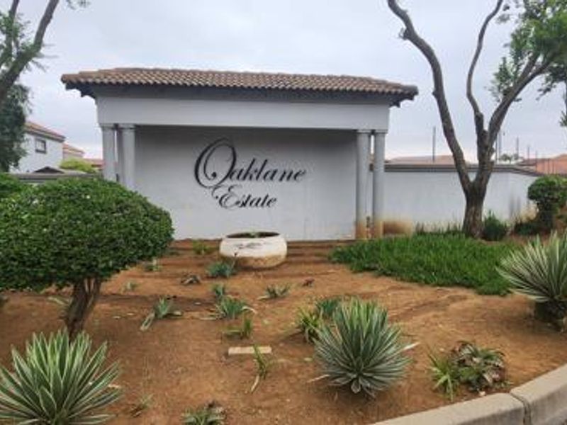The entrance to Oaklane Estate featuring a prominent signage wall, landscaped garden beds, and paved access road.
