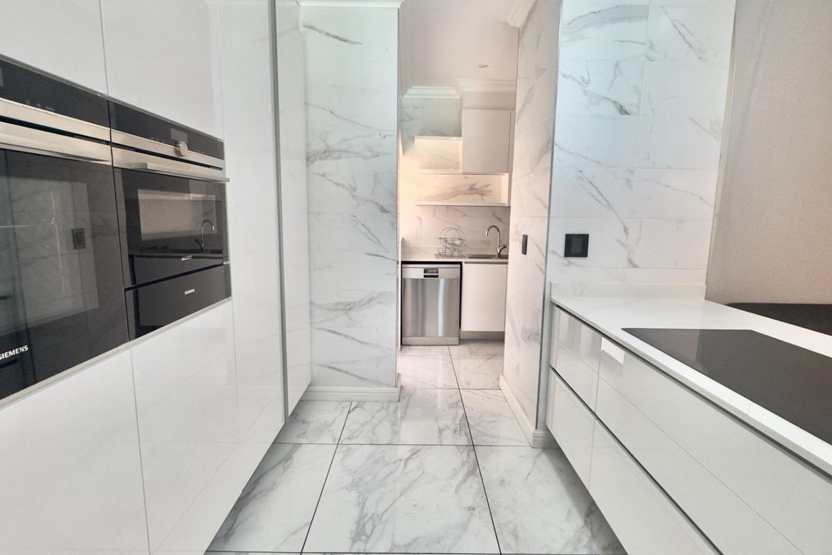 Modern kitchen featuring high-gloss cabinetry, marble-look tiled walls and flooring, integrated Siemens ovens, and a separate scullery area with additional sink and dishwasher.