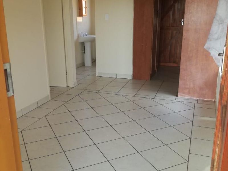 A spacious, empty hallway featuring neutral tiled flooring, built-in wooden cabinetry, and access to an adjacent bathroom area.