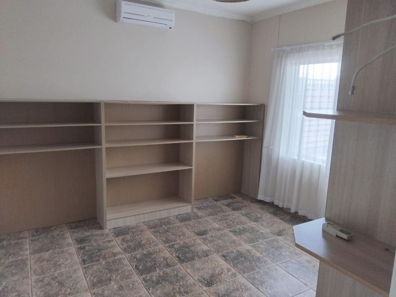 A bedroom featuring built-in shelving units, tiled flooring, and a wall-mounted air conditioning unit.