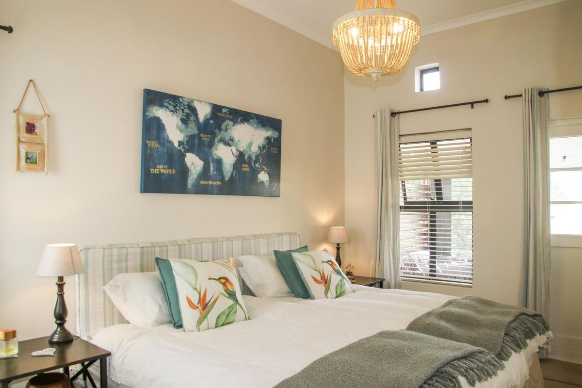 A well-maintained bedroom featuring neutral walls, a high ceiling with a decorative chandelier, and a window fitted with horizontal blinds.