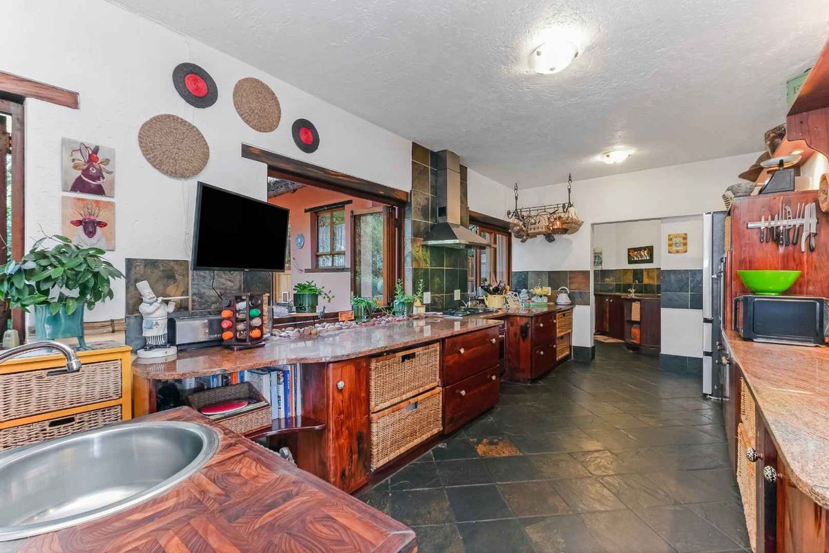 Spacious kitchen featuring granite countertops, dark slate flooring, built-in wooden cabinetry, and a stainless steel extractor fan, with an adjacent scullery area.