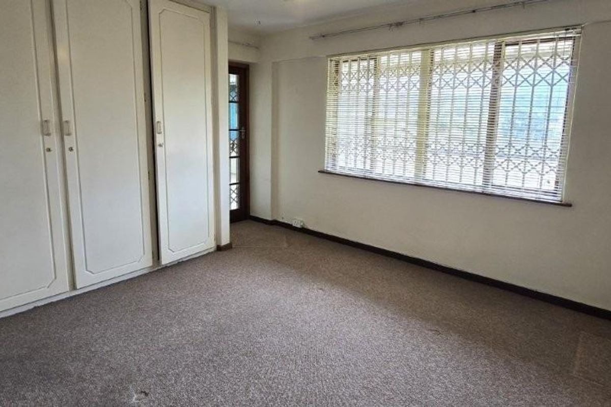 An empty bedroom featuring built-in cupboards, carpeted flooring, and windows fitted with security bars.