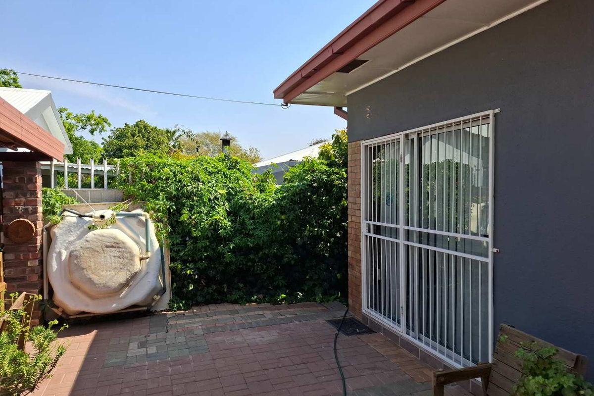 A rear patio area featuring brick paving, a security gate, and a water storage tank, set against a backdrop of established garden greenery.