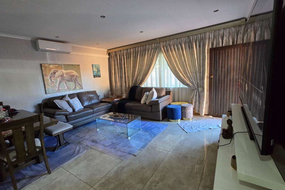 A spacious living room featuring tiled flooring, recessed downlighting, and a wall-mounted air conditioning unit, providing a comfortable and functional living space.