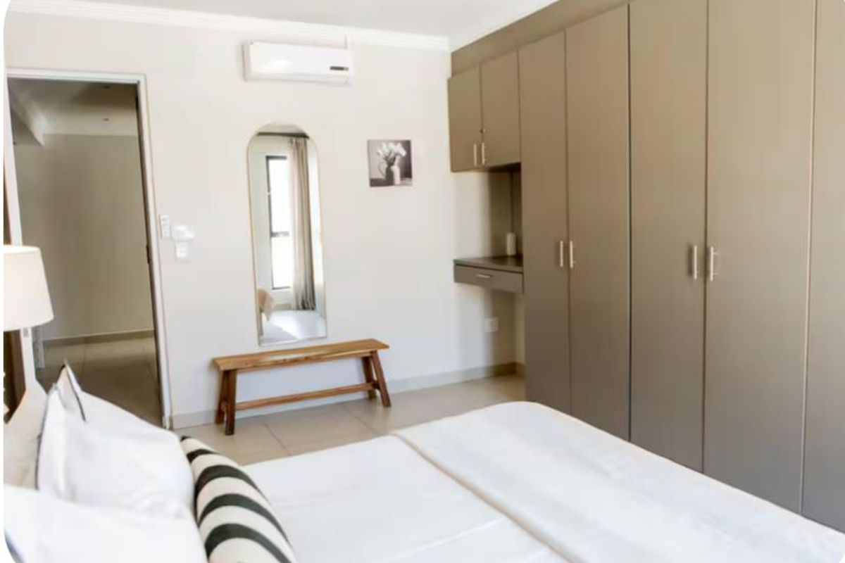 A well-maintained bedroom featuring extensive built-in cabinetry, a dedicated vanity area, and a wall-mounted air conditioning unit.