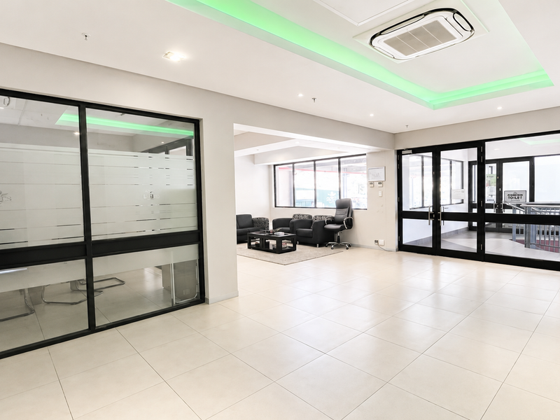 Modern open-plan office space featuring glass partitions, tiled flooring, recessed ceiling lighting, and integrated cassette air conditioning.