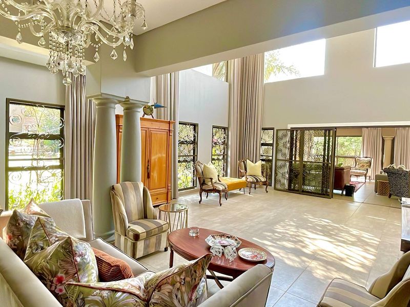 Spacious double-volume living area featuring decorative columns, large windows, tiled flooring, and elegant wrought iron security gates leading to an adjoining space.