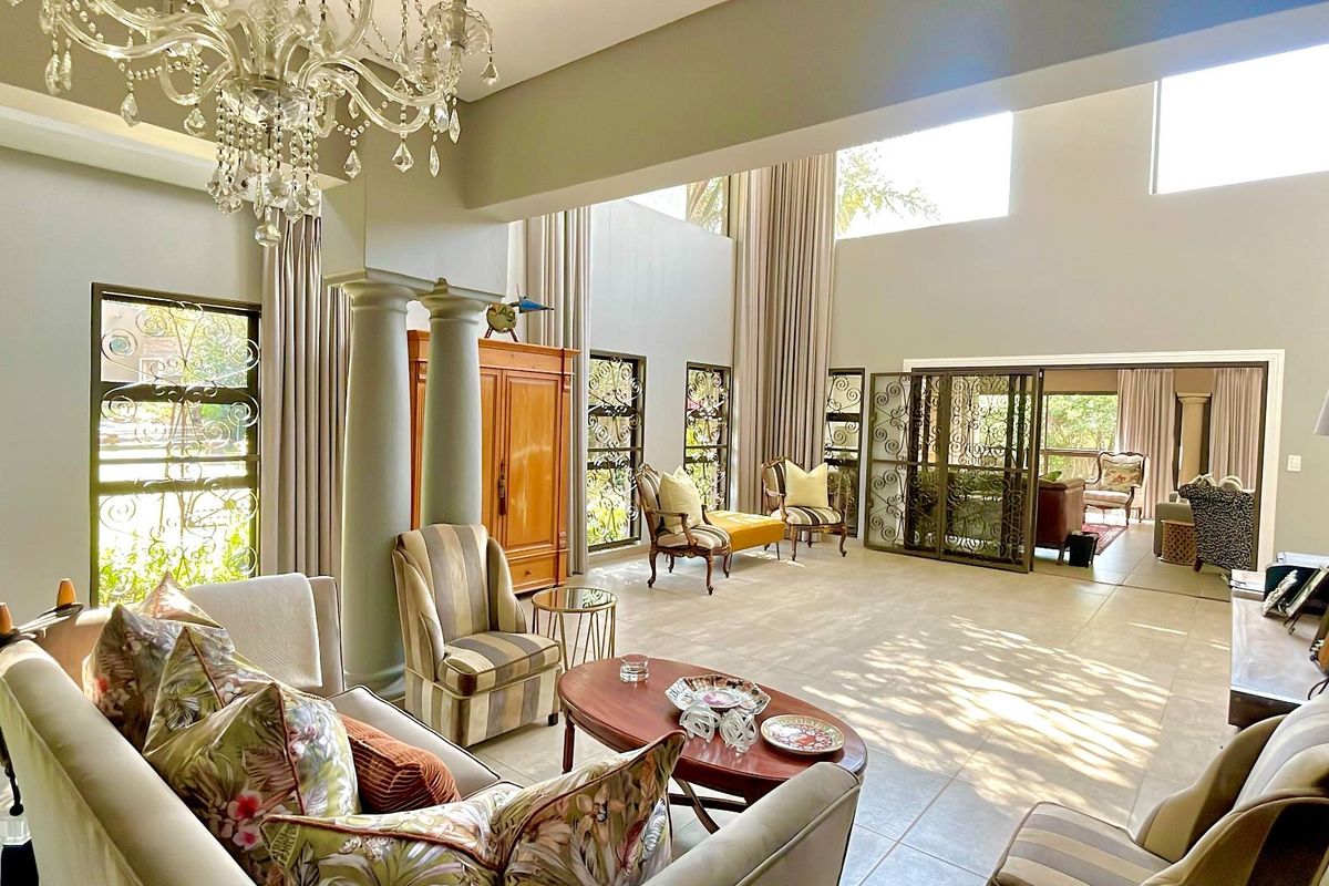 Spacious double-volume living area featuring decorative columns, large windows, tiled flooring, and elegant wrought iron security gates leading to an adjoining space.