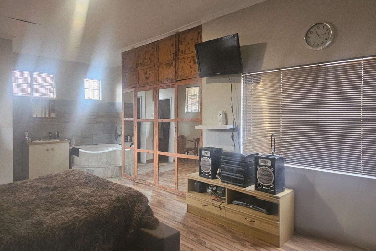 Spacious bedroom featuring integrated floor-to-ceiling wooden wardrobes and an open-plan en-suite bathroom area with a built-in corner bathtub.