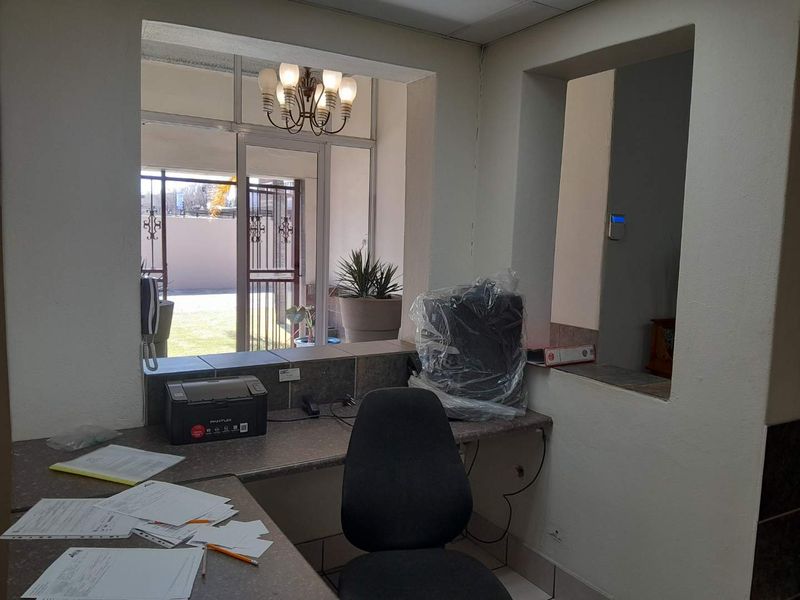 A functional office reception area featuring a built-in service counter, security alarm system, and direct access to an outdoor area through a security gate.