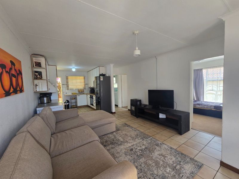 Open-plan living area featuring tiled flooring and a functional kitchen with built-in cabinetry, seamlessly connecting to the adjacent living space.
