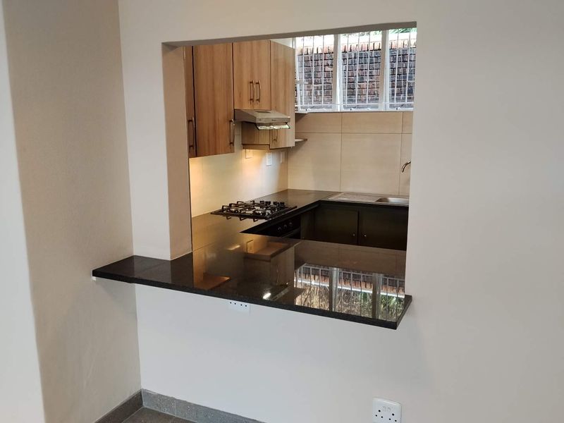 A functional kitchen featuring granite countertops, a gas hob, built-in oven, and wooden cabinetry, viewed through a convenient breakfast bar opening.